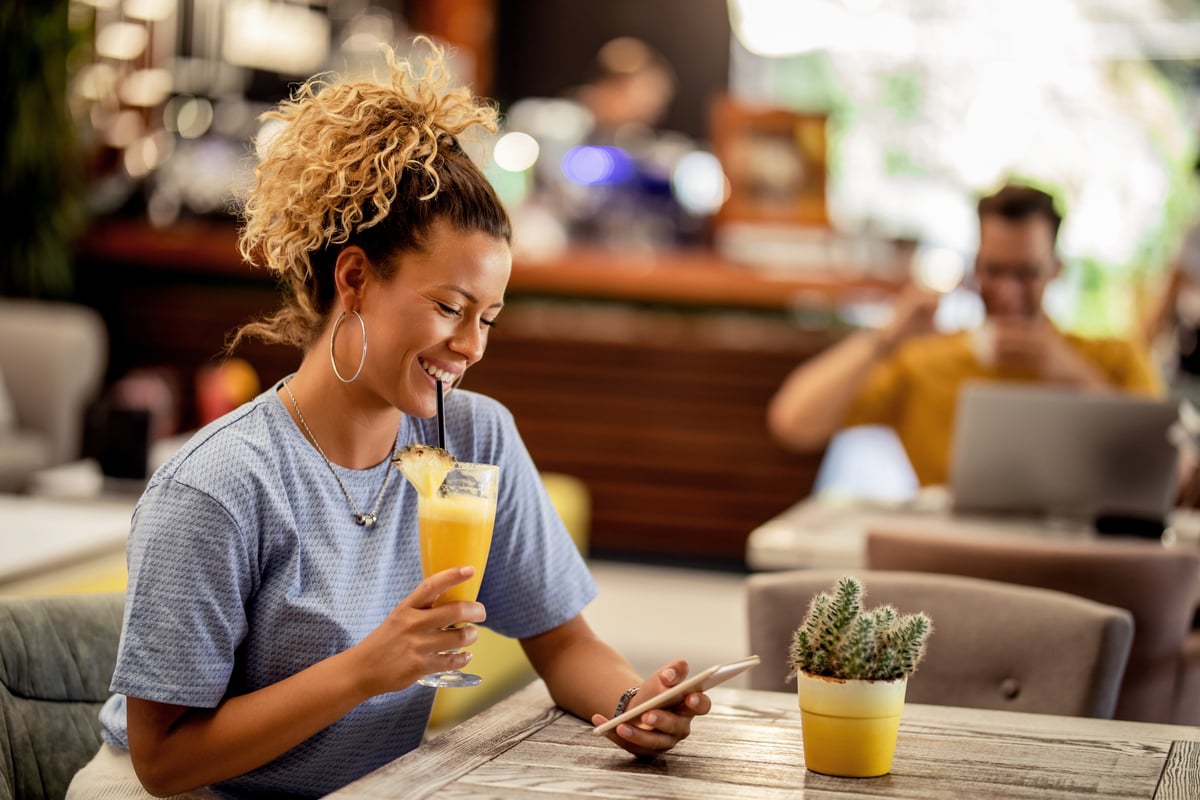 Woman drinking a glass of juice and looking at a phone.