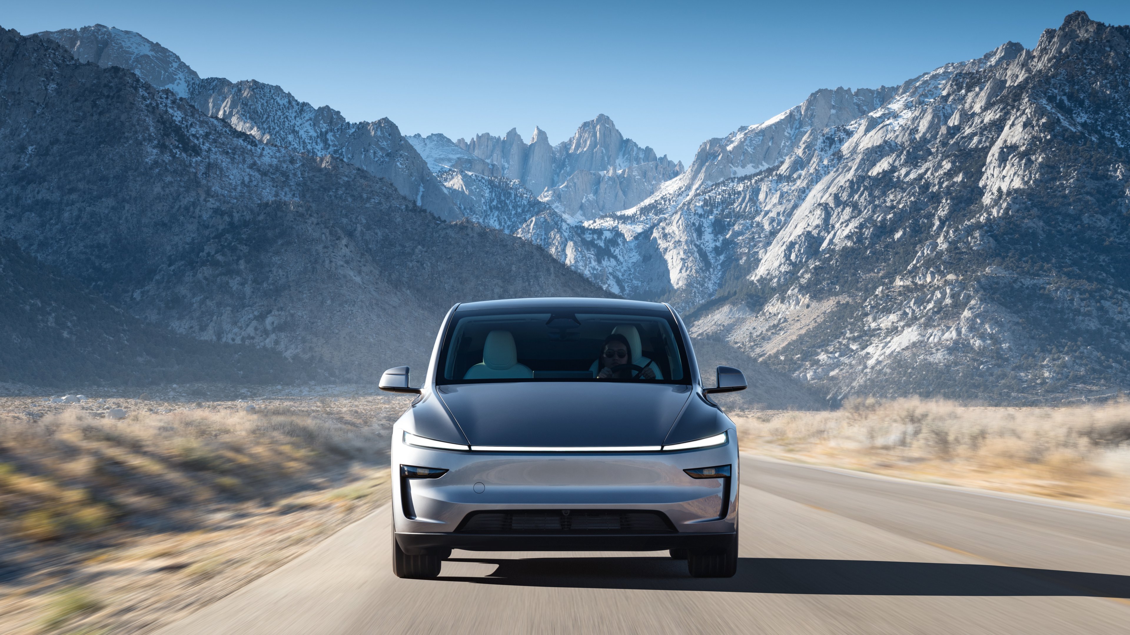 New Model Y with front light bar driving with snowy mountains in the background.