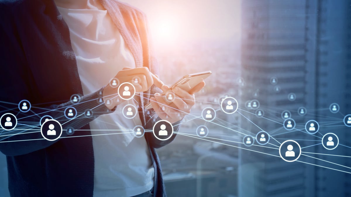 A digital network of icons is displayed around a person using a smartphone.