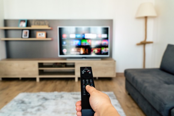 A person holding remote in their right hand and pointing to a TV.