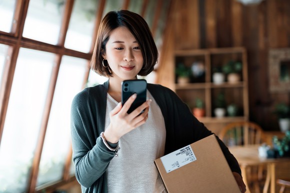 Person holding a delivery box and looking at a smartphone.
