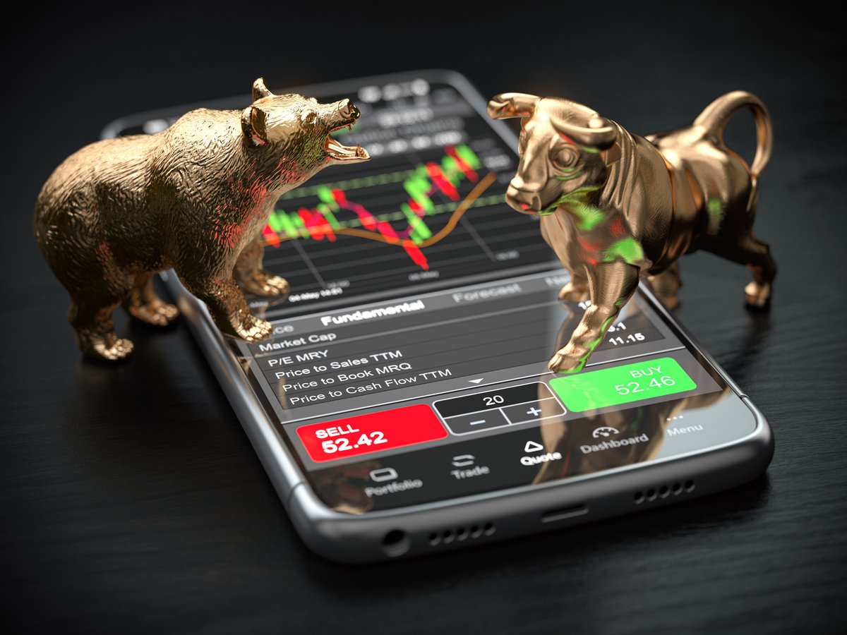 Bear and bull figurines standing on a smartphone with a stock app displayed.