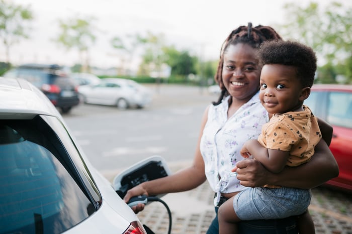 A parent carrying a child while charging an electric car.