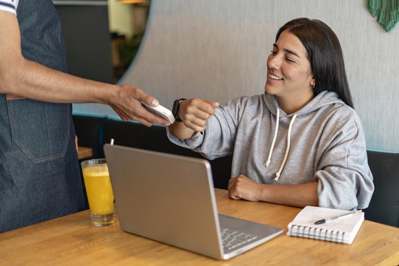 Woman at computer makes payment using smartwatch. 