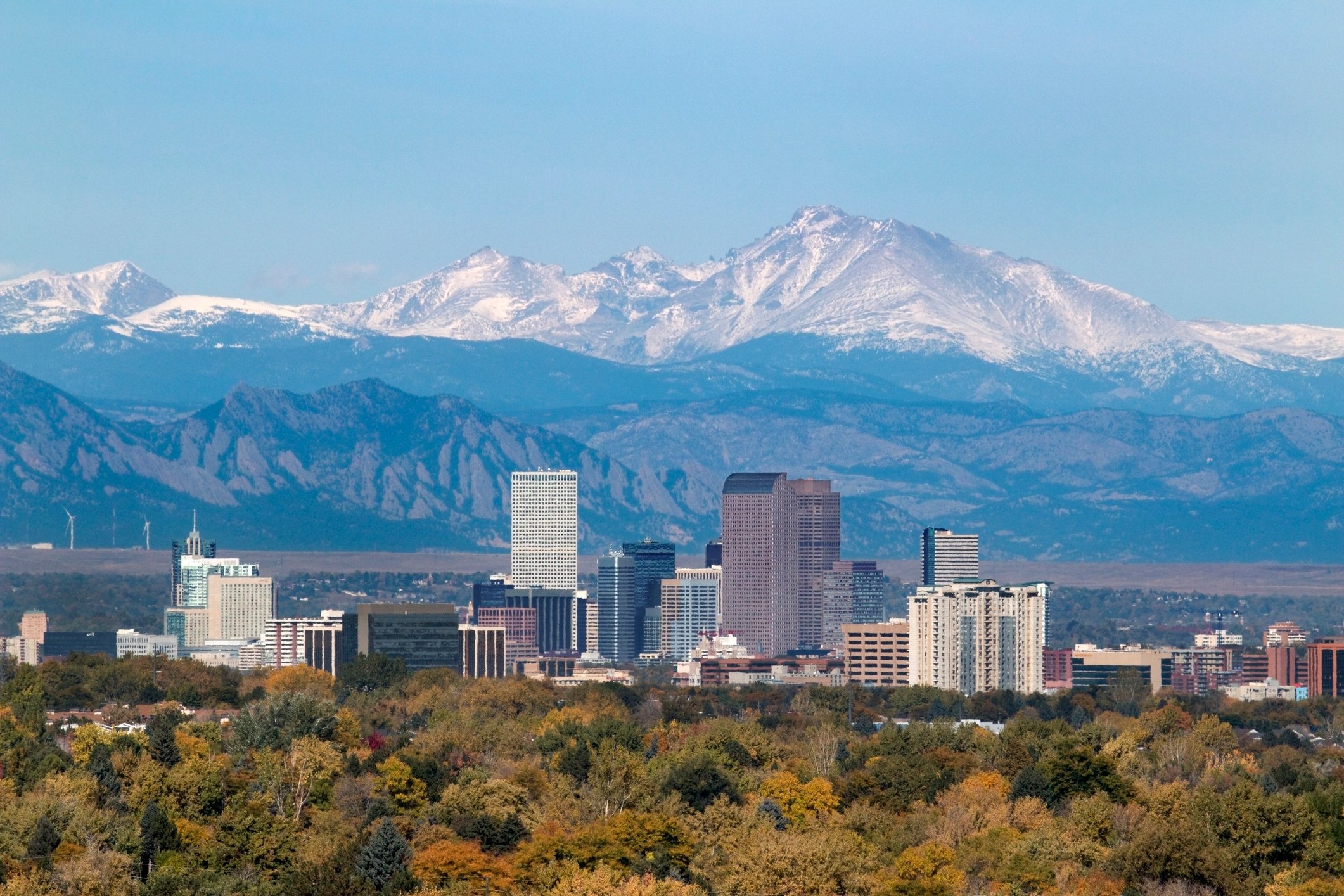 A city is shown, in front of the snowy Rocky Mountains.