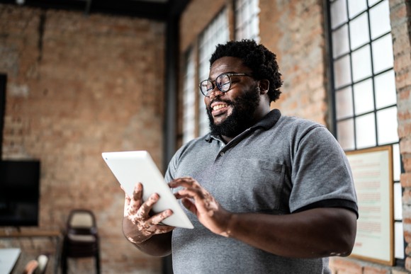 A person smiles at a tablet computer in their hands.