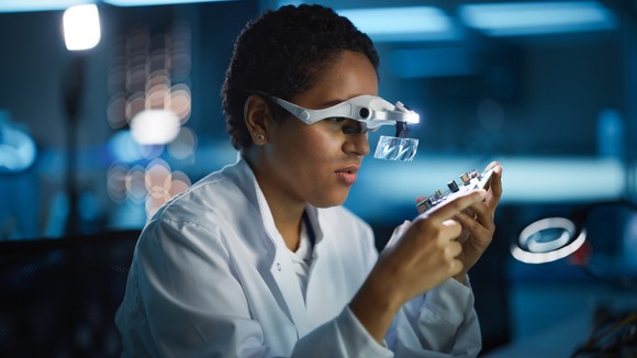 A person in a lab coat analyzing a semiconductor.