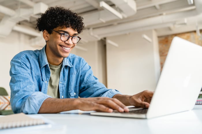 Smiling person in office, typing on a laptop.