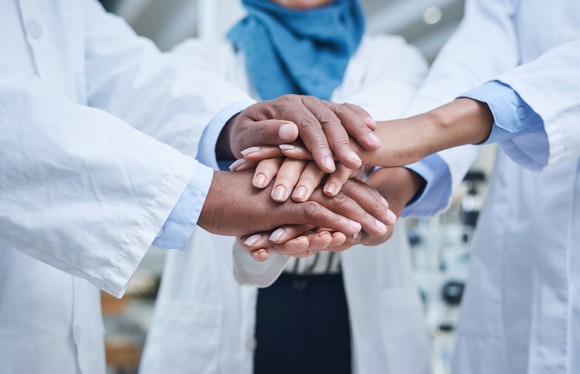 People in lab coats with hands stacked together.