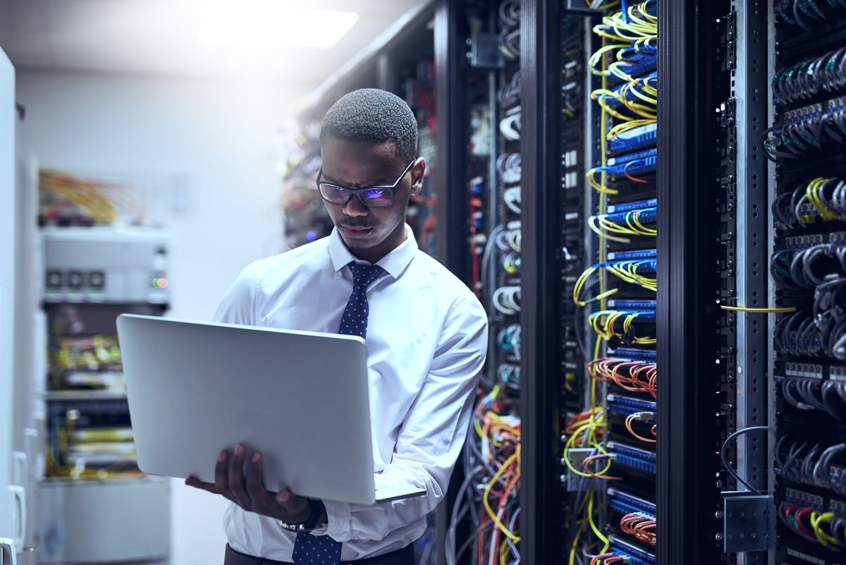 An engineer using a computer while standing next to a row of servers.