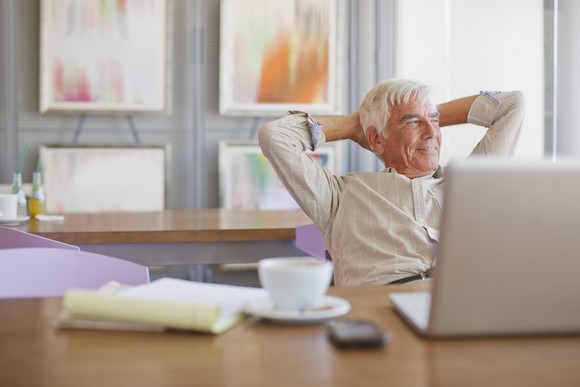 A person holding hands behind head while sitting in front of a laptop.