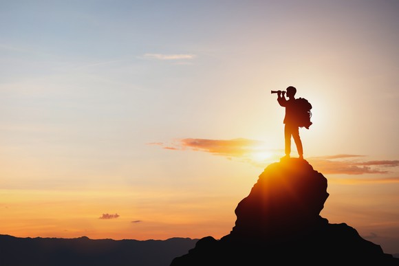 A hiker on top of a peak, looking off into the sunset.