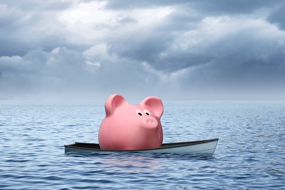 A piggy bank sits in a small boat, which is floating on water with rain clouds moving in.