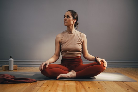 Person in yoga clothes sitting on a yoga mat, looking to the side. 