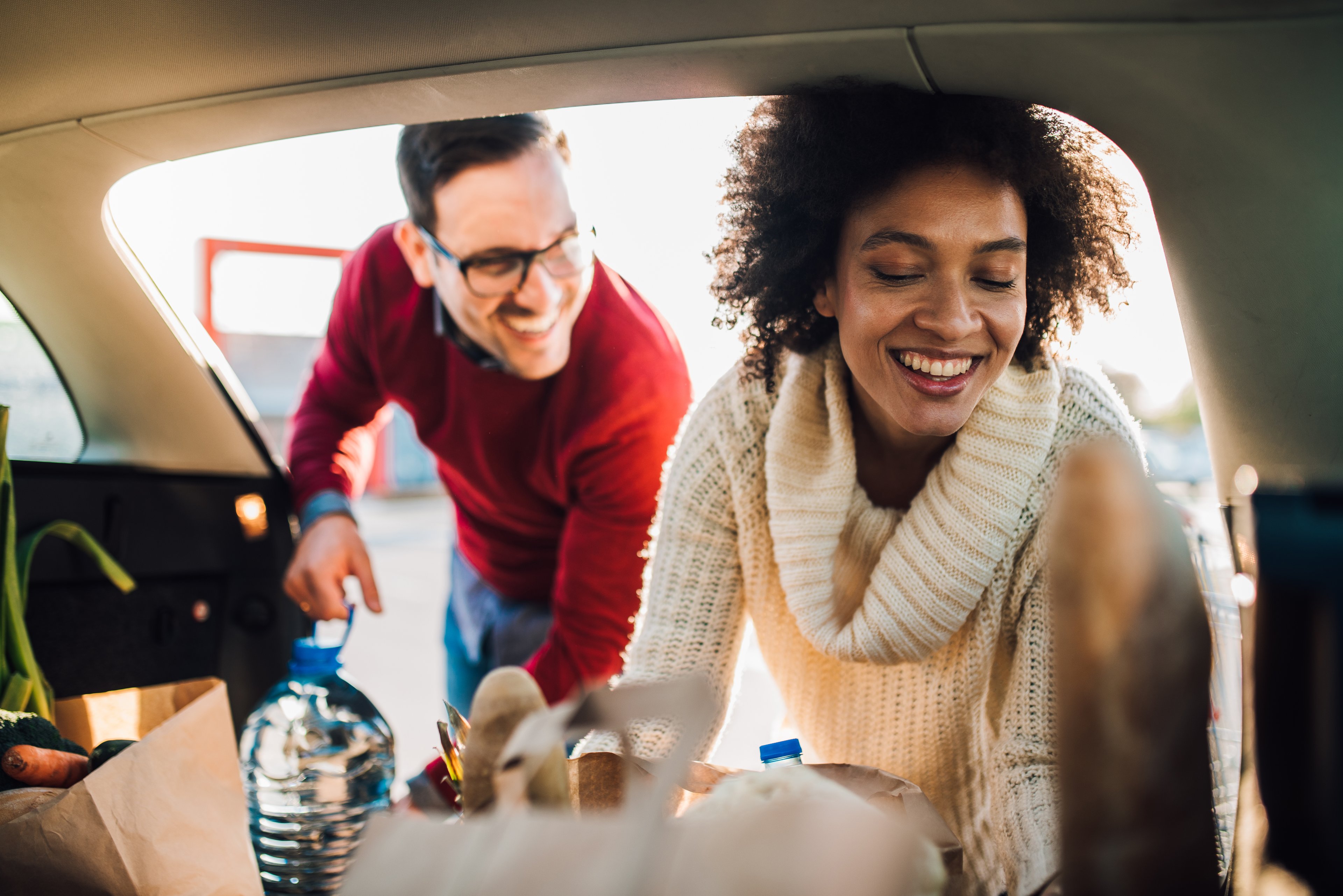 Two people load a car with groceries.