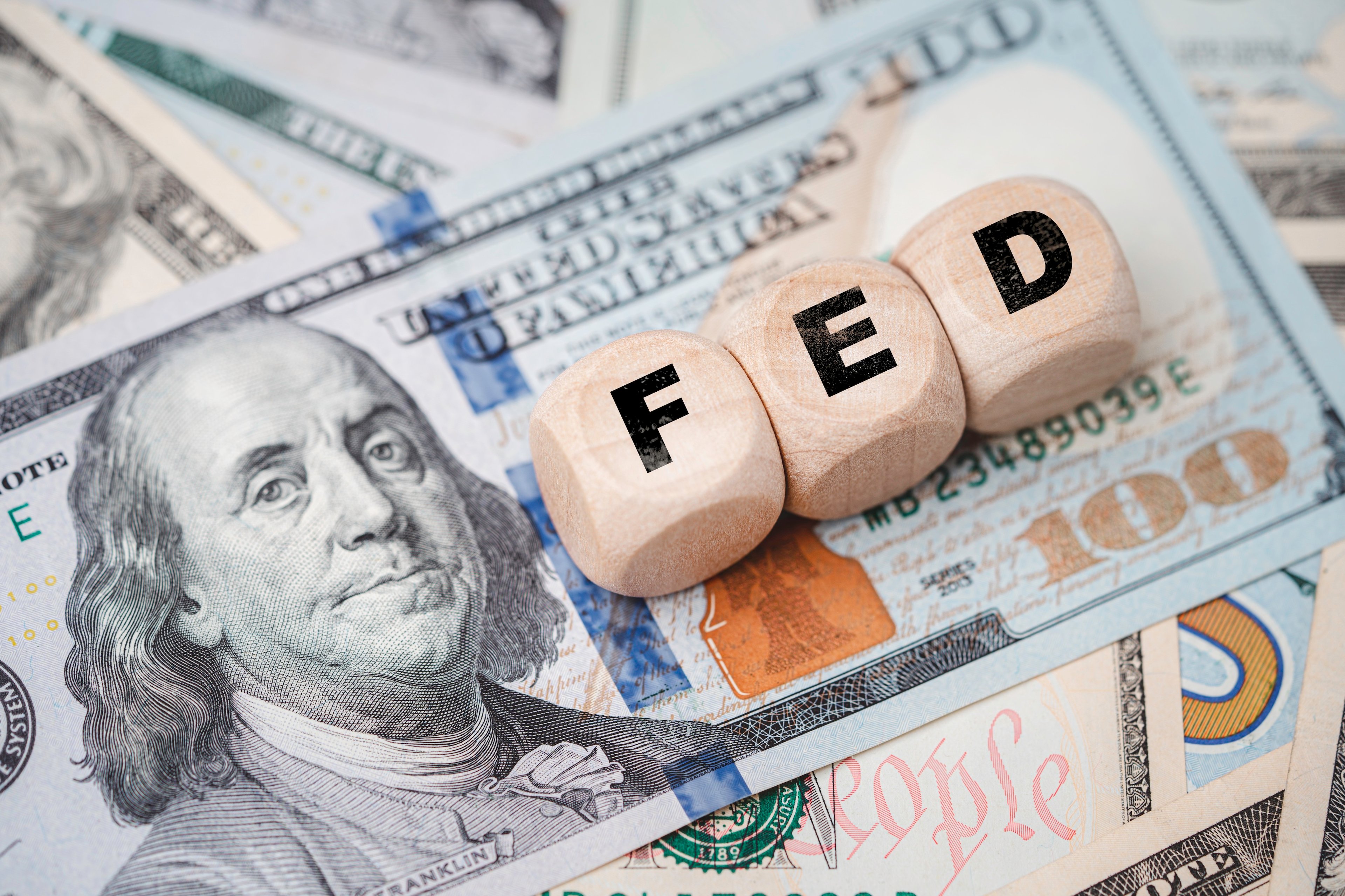 Small wooden blocks labeled "FED" sit on top of a $100 bill.