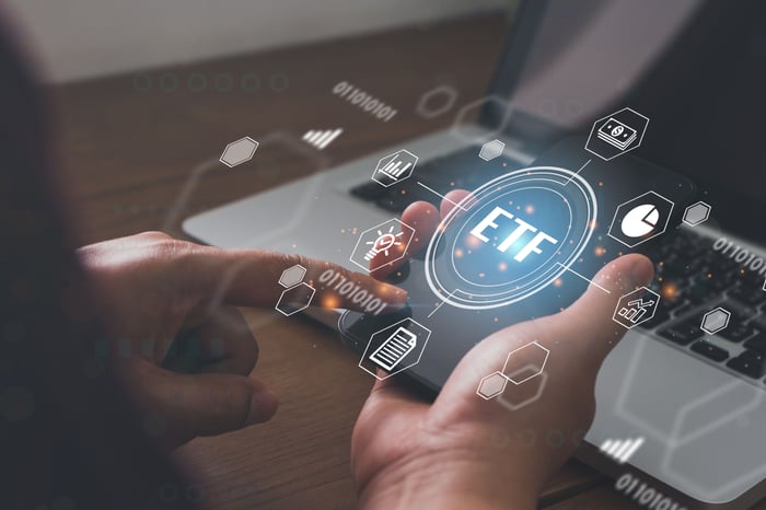 Person at laptop holds virtual graphic depicting ETF.