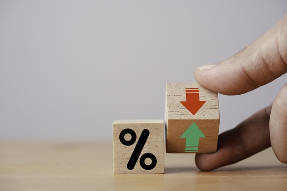 A hand turning wooden blocks showing a percentage symbol and arrows pointing up and down.