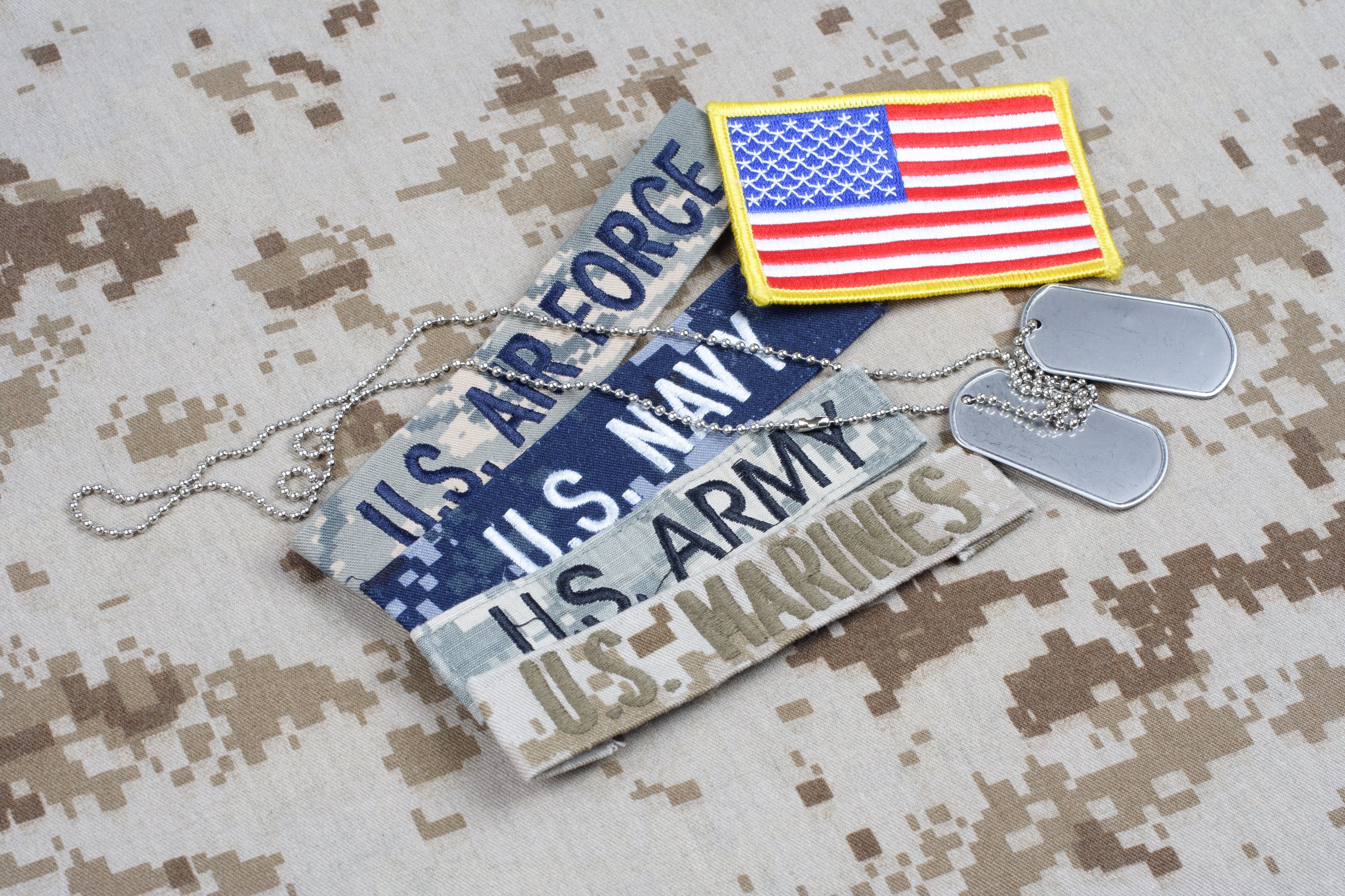 An American flag patch, dogtags, and pieces of uniform from the Air Force, Navy, Army, and Marines.