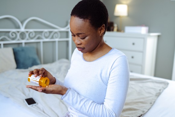 A person sitting on their bed while preparing to take prescription pills. 