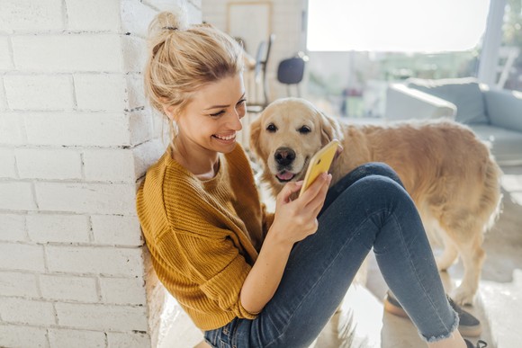 A person scrolls through their phone while sitting on the floor next to their dog.