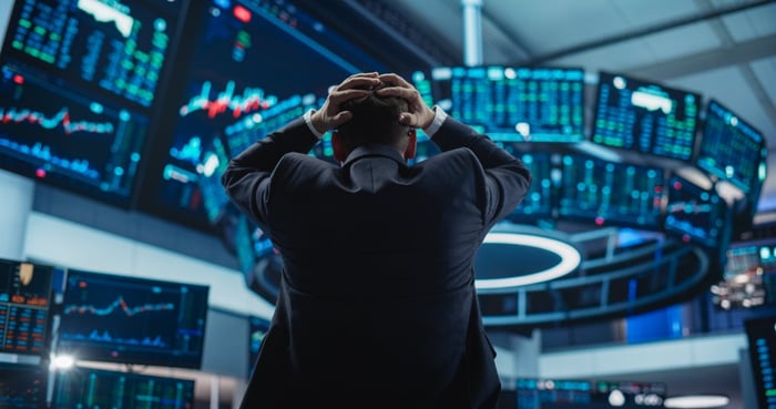 A stock trader stands with hands on head while watching market results roll in. 