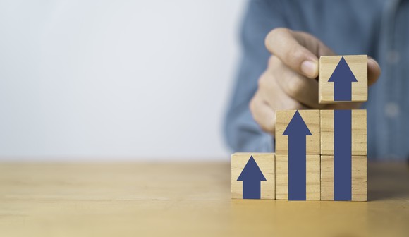 A person stacking blocks that show progressively larger upward-pointing arrows.