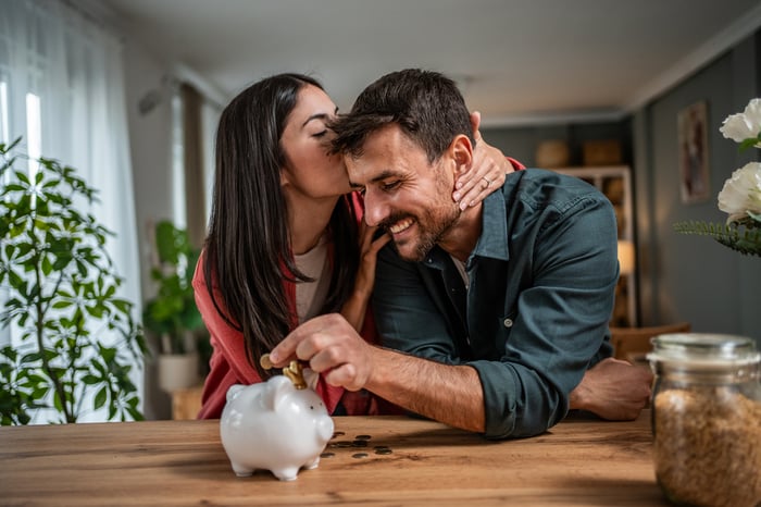 Person kissing other person as they put a coin in a piggy bank.
