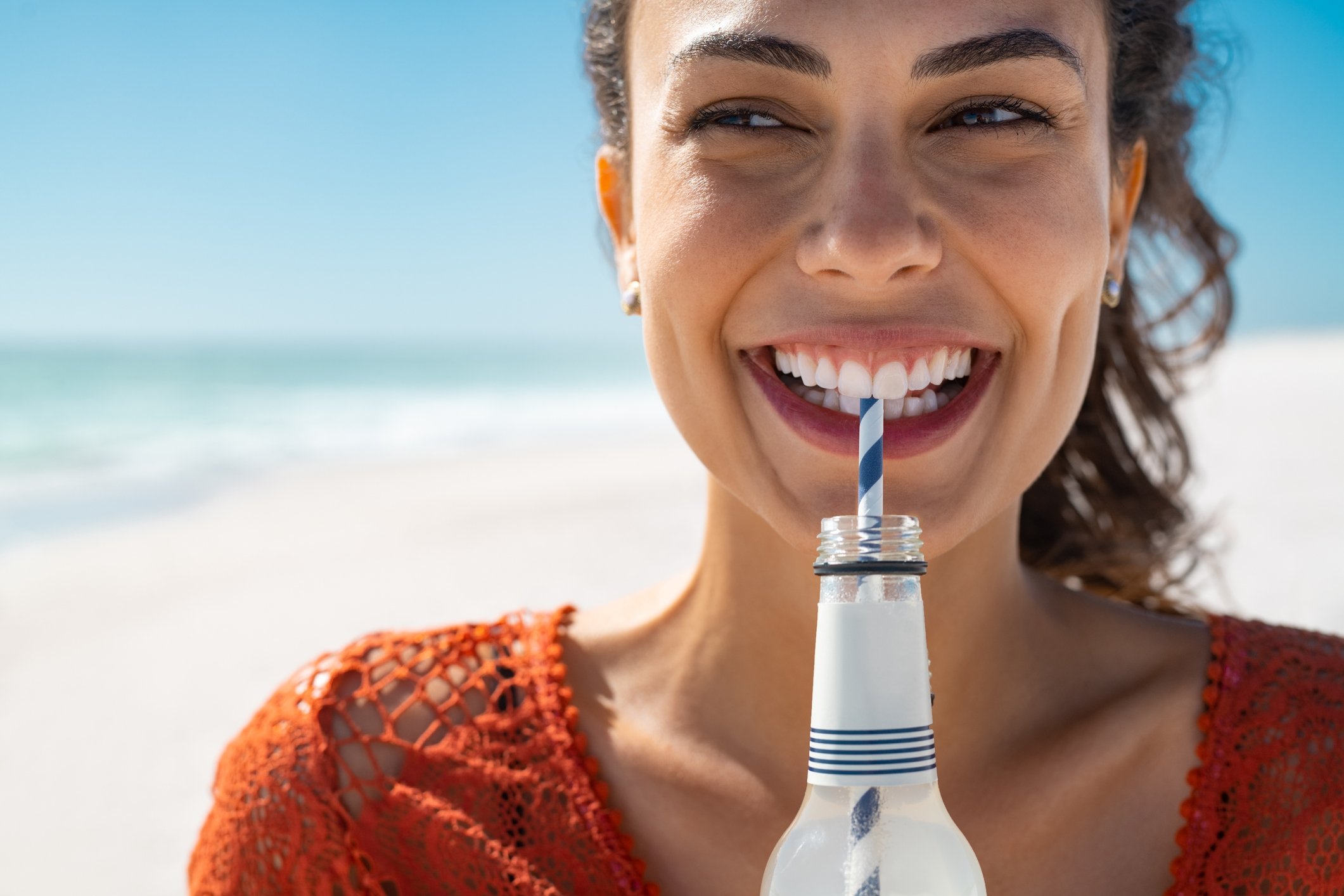 Someone on a beach sipping soda out of bottle through a straw.