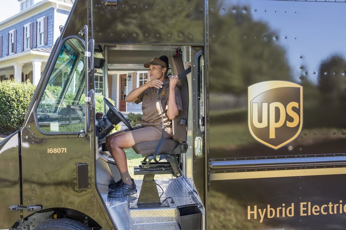 UPS delivery driver sitting in a brown hybrid electric truck.