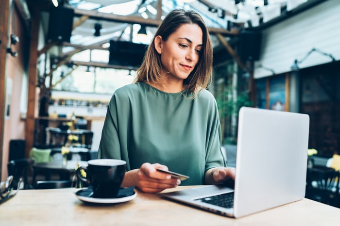 Person holding card and looking at a laptop.