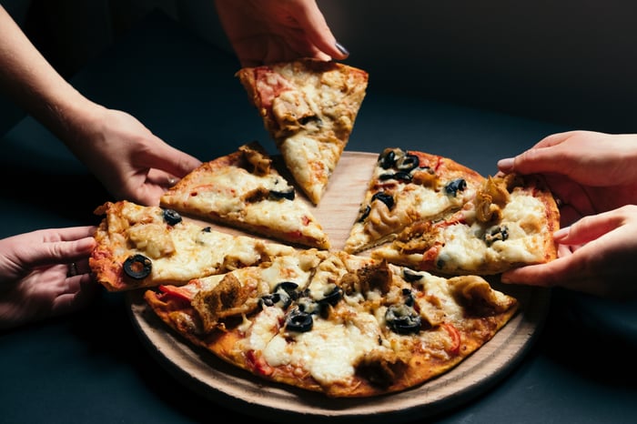 A few hands grabbing pizza. 