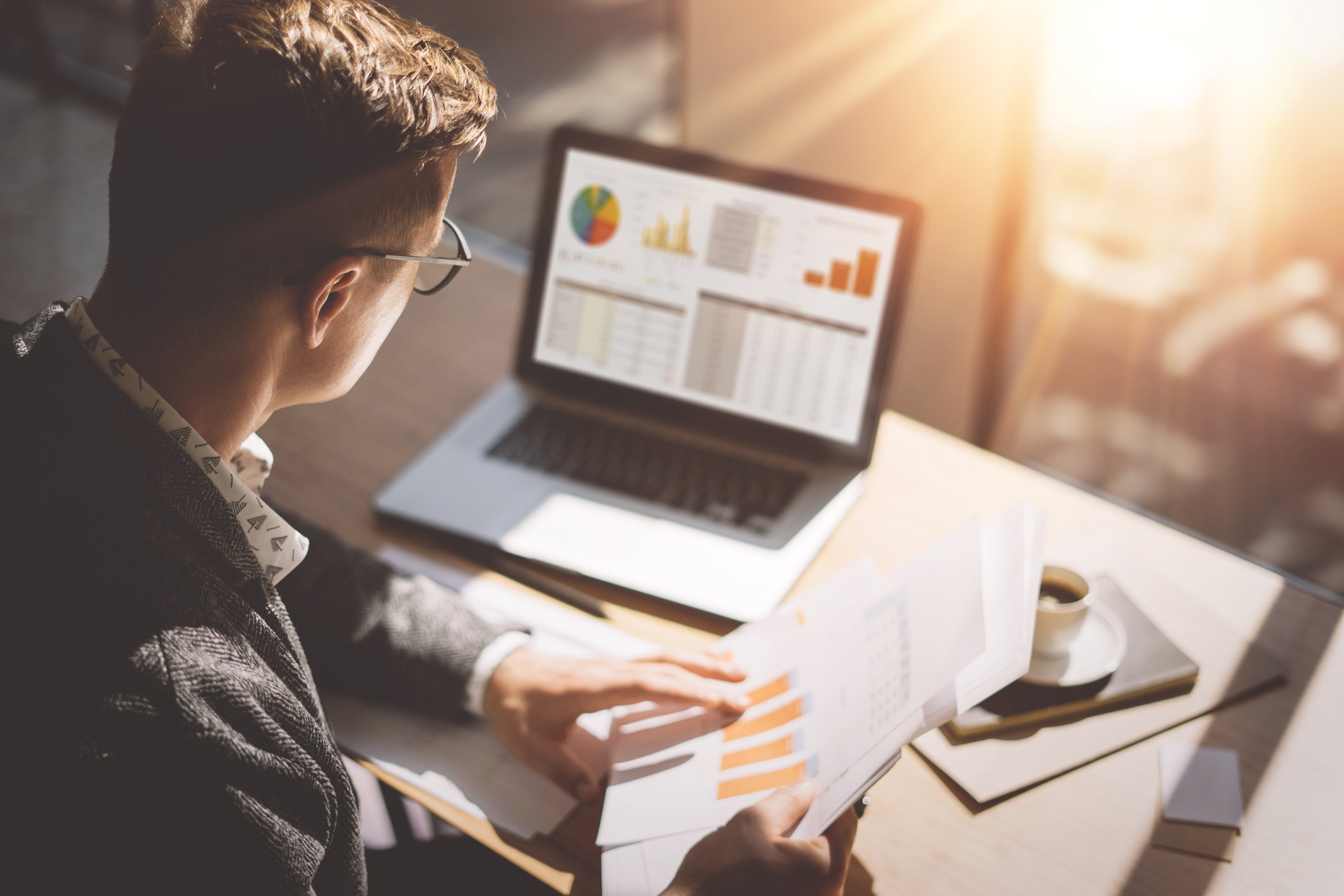 An investor holds paper documents while looking at his computer screen.