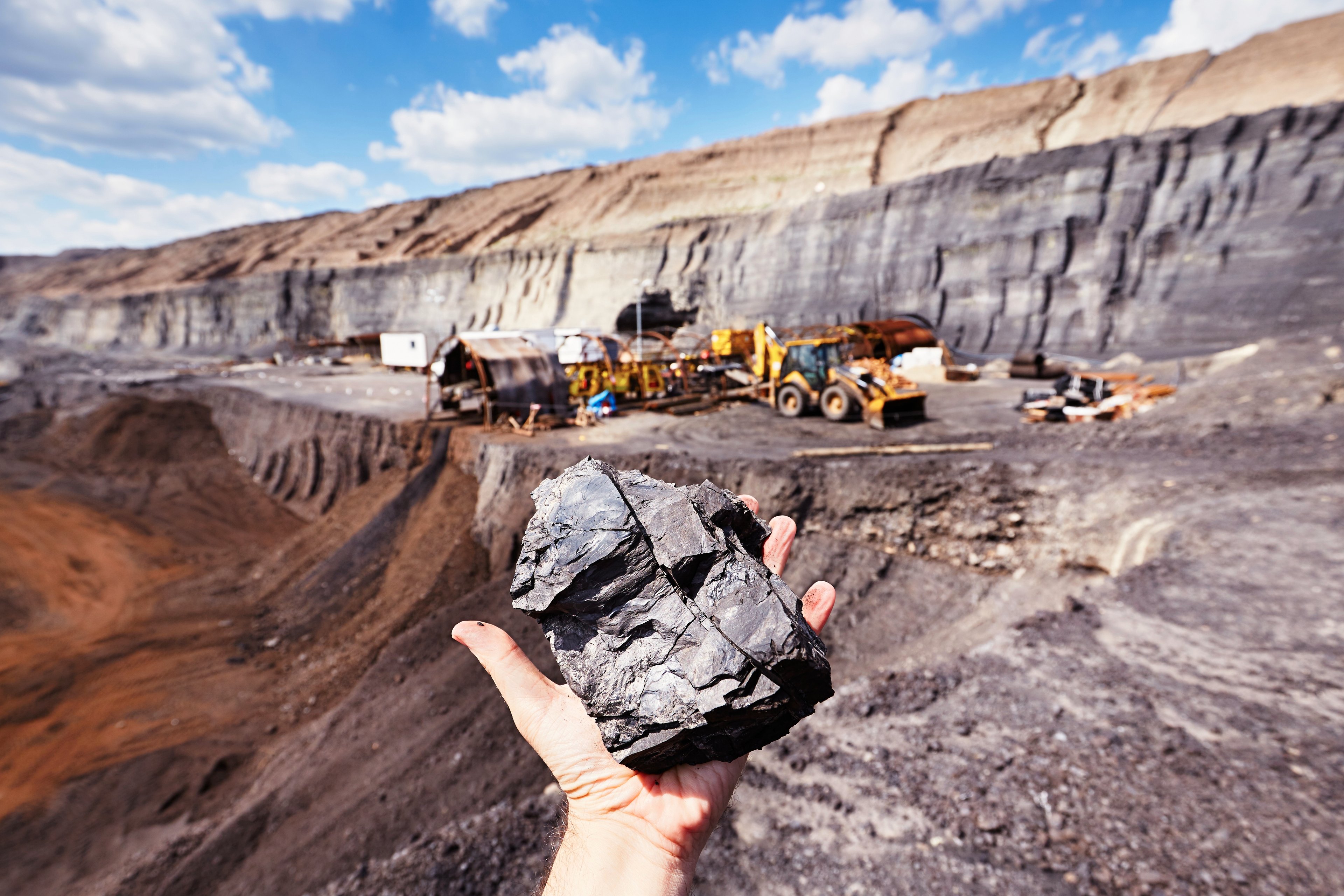 Hand holding a mineral in the foreground of a mining operation. 
