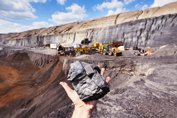 Hand holding a mineral in the foreground of a mining operation. 