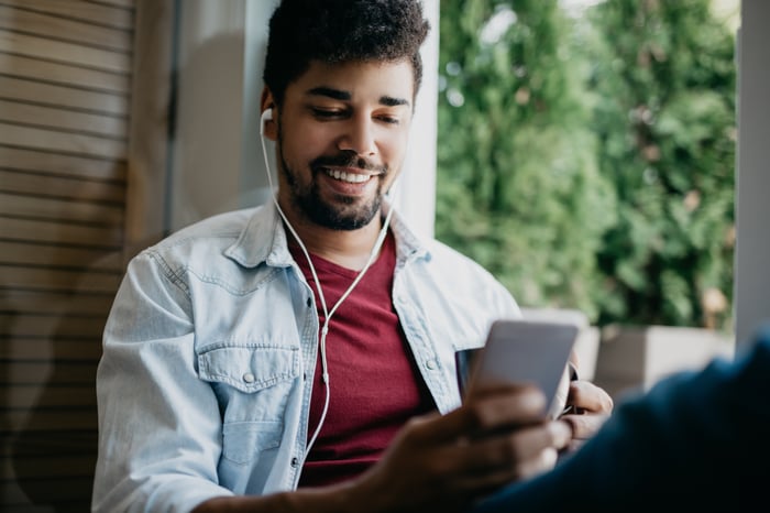 Young investor with earphones smiles at smartphone. 