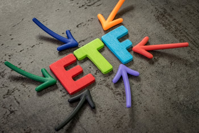 Colorful wooden letters spelling ETF surrounded by multicolored arrows pointing inward.