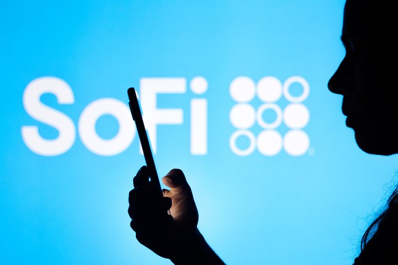 SoFi logo behind the silhouette of someone holding up their phone.