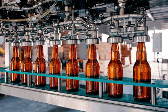 Beer bottles being filled by machine at brewery.