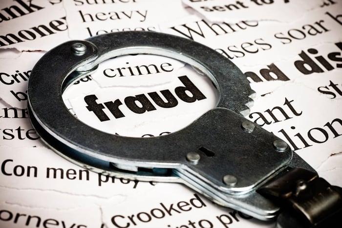 Pair of handcuffs sitting atop newspaper clippings about fraud. 