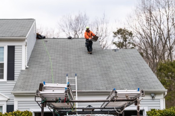 Contractor carrying a shingle down a roof. 