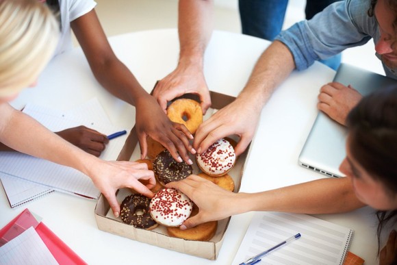 People reaching for donuts at an office.