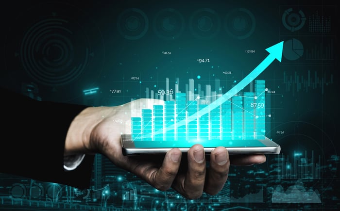 A line going up over an ascending bar chart held by a person.