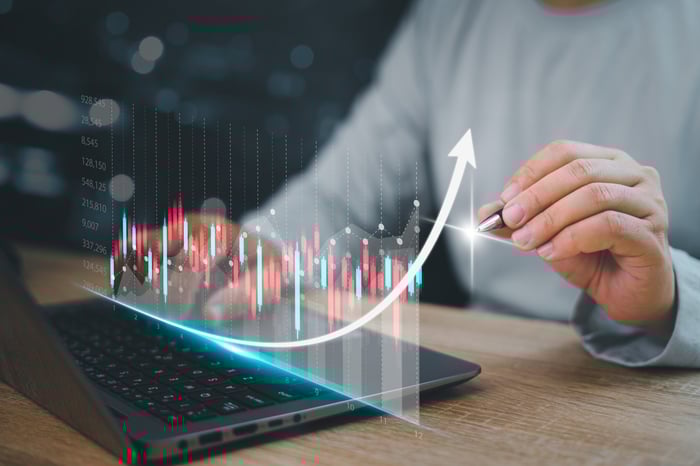 Person at laptop with graphics showing stock performance and an upward arrow.