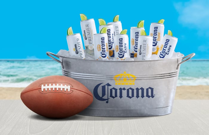 A bucket of Coronas on a beach next to a football.