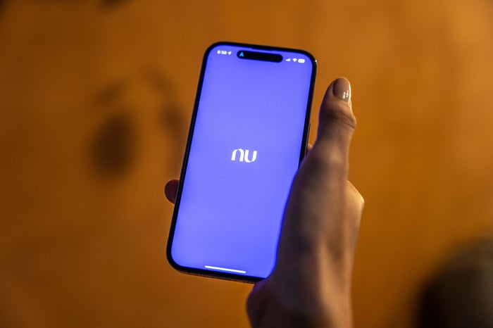 A hand holding a smartphone displaying the Nu app.