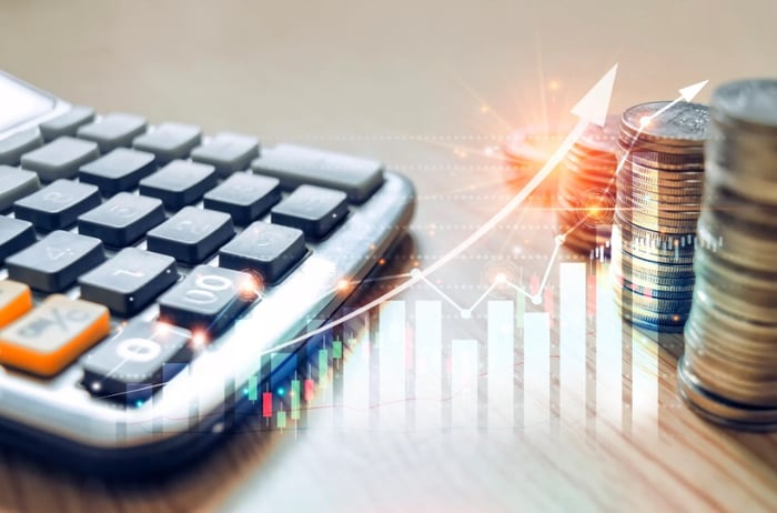 An arrow surging upward between a calculator and stacks of coins.