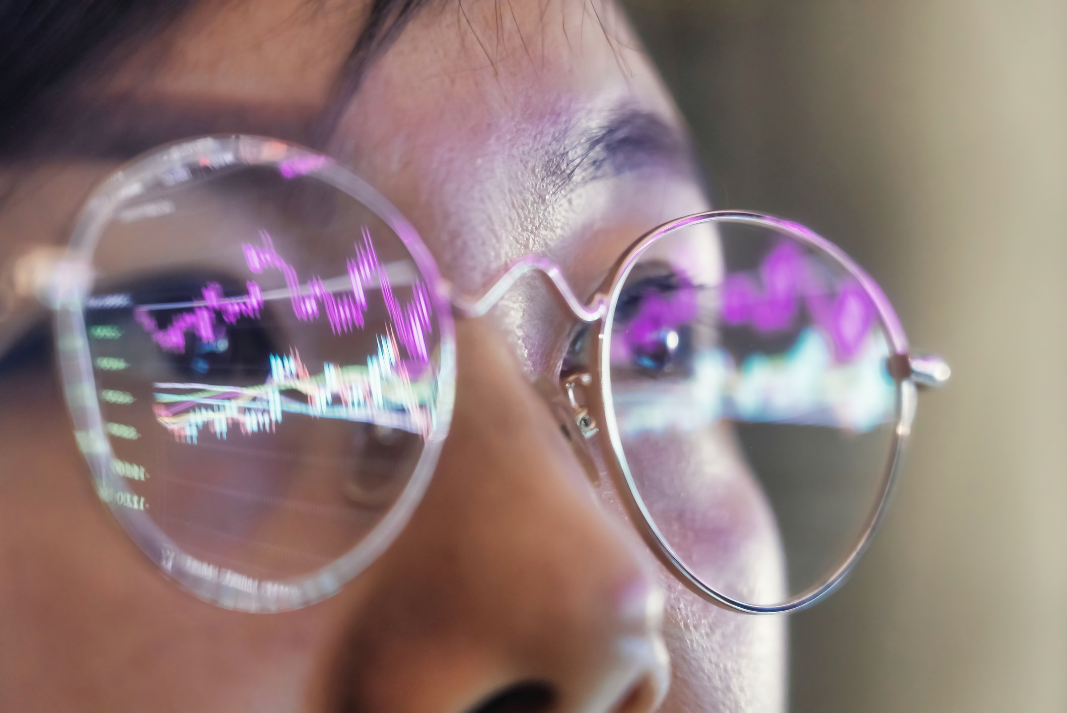 A person wearing glasses that are reflecting stock charts.
