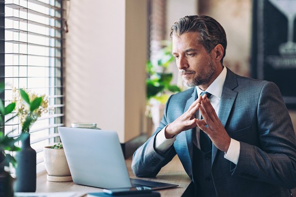 A person wearing a suit looks at a computer with a contemplative expression.