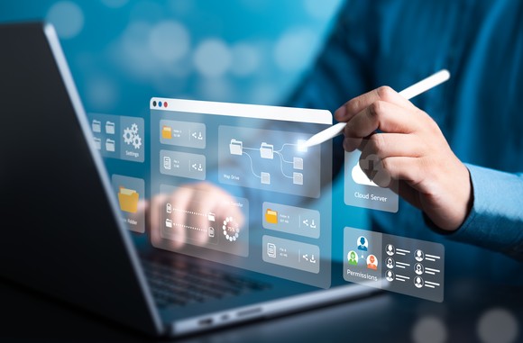 I hand holds a stylus and selects an icon that is displayed in front of a laptop.